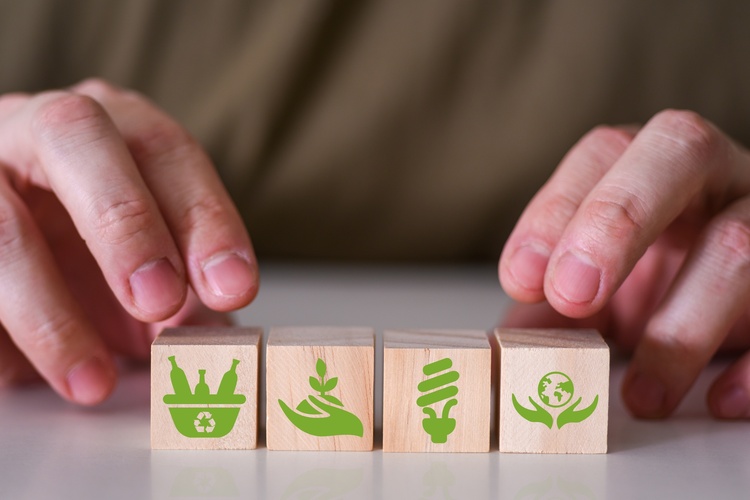 Två händer placerar träklossar med gröna miljöikoner på ett bord.