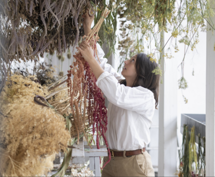 Person hänger upp torkade blommor i ett ljust rum fyllt med växter.