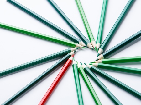 Flera gröna och en röd färgpenna ligger i en cirkel på ett vitt underlag.