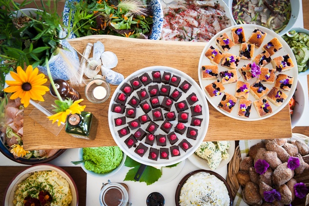 Ett bord dukat med olika färgglada maträtter och desserter, dekorerat med blommor och gröna växter.