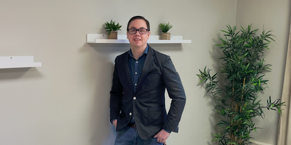 En person står vid väggen i ett mötesrum med bord, stolar, växter och hyllor med krukväxter.