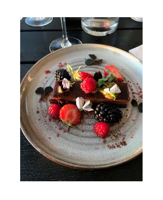 En elegant dessert med choklad, färska bär och ätbara blommor på en tallrik.