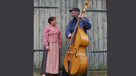 Två personer står framför en trävägg, en spelar kontrabas och den andra tittar på.