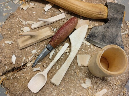 Träslöjdsverktyg och träföremål på en trästubbe med träspån runtom.