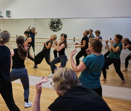 En grupp kvinnor deltar i en dans- eller träningsklass framför en spegelvägg i en dansstudio.