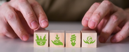 Två händer placerar träklossar med gröna miljöikoner på ett bord.