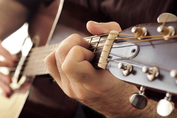 Närbild av en person som spelar akustisk gitarr, fokus på vänster hand på gitarrens greppbräda.