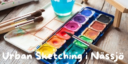 Akvarellfärger, penslar och ett glas vatten på ett träbord. Text: Urban Sketching i Nässjö.