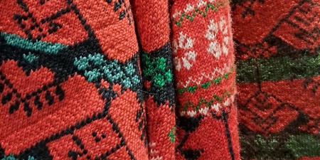 Närbild av röda stickade tröjor med traditionella delsbomönster i grönt, vitt och svart.