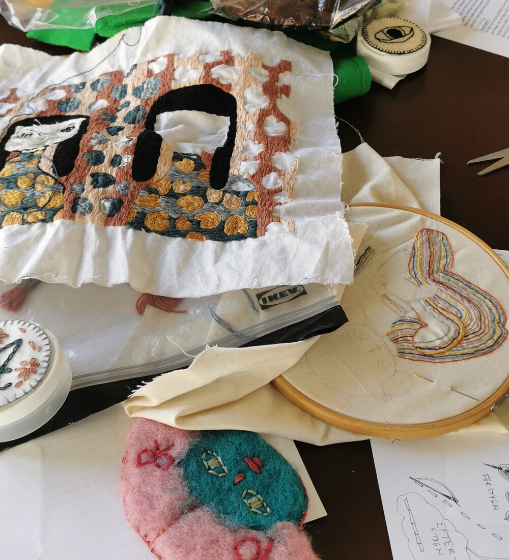 Ett bord med broderimaterial, färdiga och pågående broderier, tygbitar och en broderibåge.