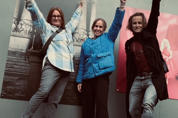 Angela Karlsson, Anna Sellén, Richard Forsberg står framför affischer och poserar med ena armen uppsträckt, leende mot kameran.