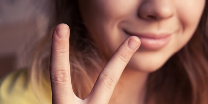 En person i gul tröja visar ett V-tecken med handen och har färgglada armband på handleden.