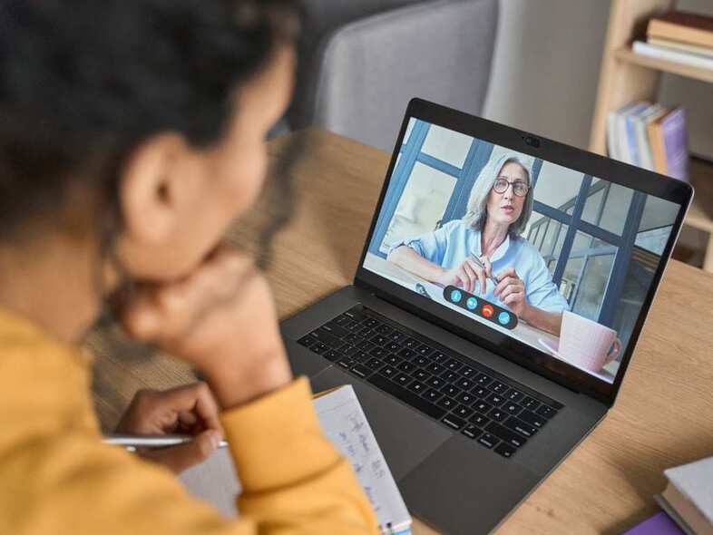 Kvinna i gul tröja sitter och har ett digitalt möte på laptopen.