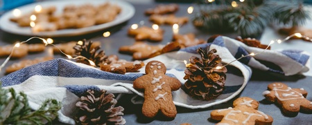 Pepparkakor dekorerade med glasyr ligger på ett bord med kottar, granris, tygservett och julbelysning.