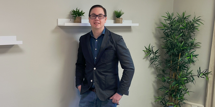 En person står vid väggen i ett mötesrum med bord, stolar, växter och hyllor med krukväxter.