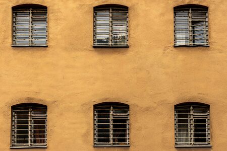 Sex fönster med galler på en gul putsad fasad, ordnade i två rader om tre.