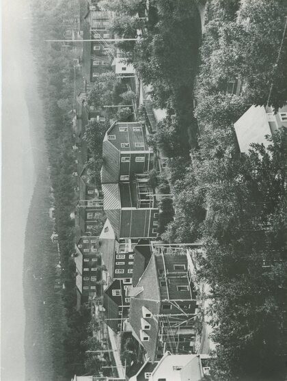 Svartvit bild av en småstad med trähus, träd och skog i bakgrunden.