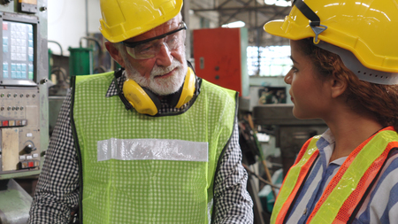 Två personer med skyddshjälm och väst samtalar i en industrimiljö.