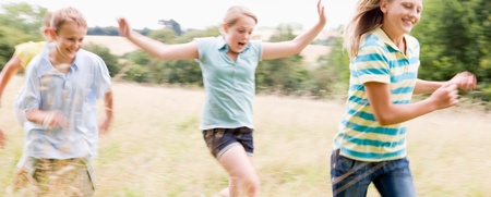 Fyra barn springer och leker i ett somrigt gräsfält med träd i bakgrunden.