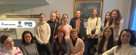 Gruppfoto av 15 personer, mestadels kvinnor, sittande och stående i ett rum med tavla och logotyper på väggen.