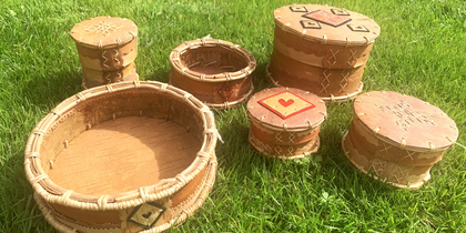 Sex traditionella runda askar av näver står på gräs i solljus.