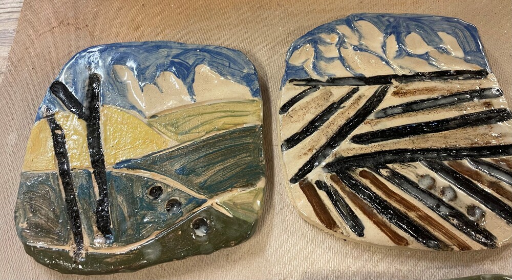 Två keramiska plattor med abstrakta landskapsmotiv i blått, grönt, gult och svart.
