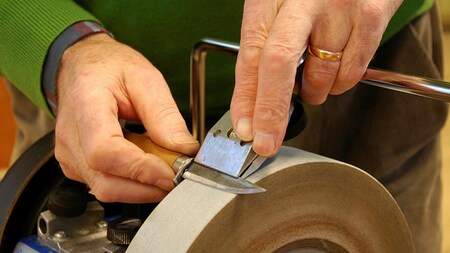 En person slipar ett stämjärn mot en roterande slipsten med händerna synliga.