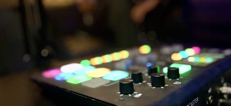 Närbild av en ljudmixer med färgglada, upplysta knappar och rattar i ett mörkt rum.