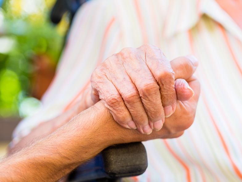 Två äldre personer håller varandra i handen, närbild med fokus på händerna.