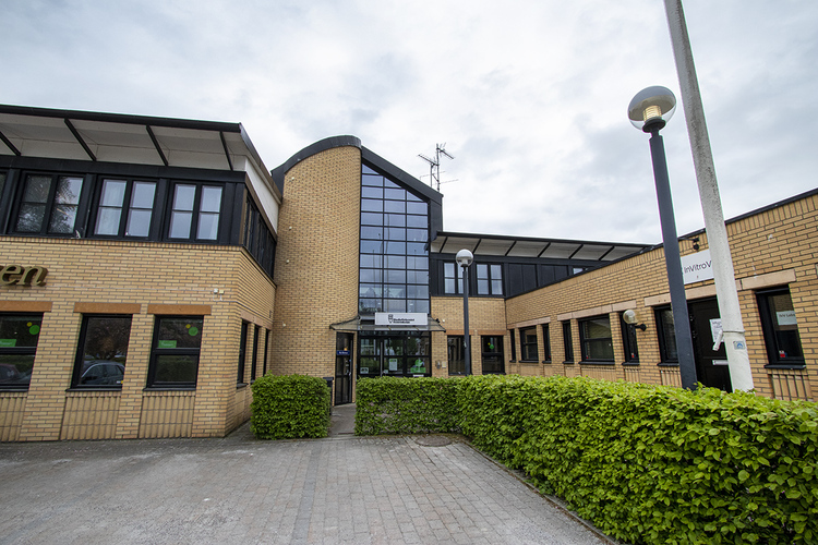 Entré till en modern byggnad med ljusgul tegelfasad, stora fönster och glasparti i mitten.