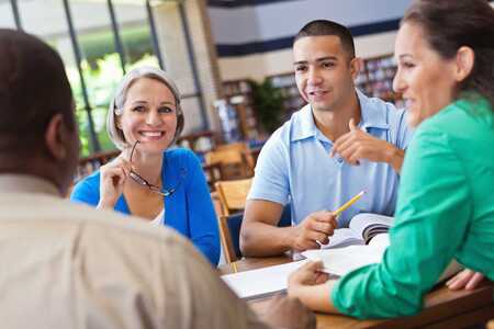 Fyra personer sitter runt ett bord i ett bibliotek och diskuterar.