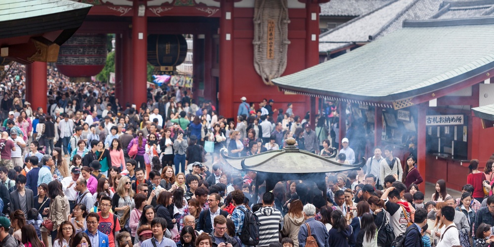 Stor folkmassa samlad vid ett tempel i Japan, med rök från en rökelsebrännare i förgrunden.