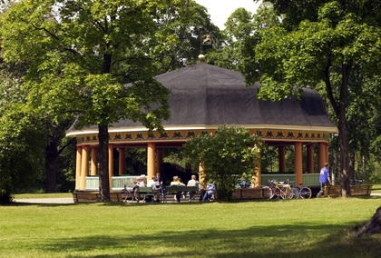 En paviljong i en grön park med människor som sitter vid bänkar och cyklar parkerade bredvid.