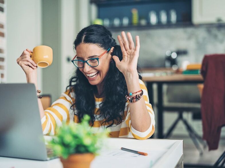 En glad kvinna framför en laptop.