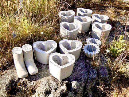 Betongformar i hjärtform och stövelform står på marken bland gräs och stenar utomhus.