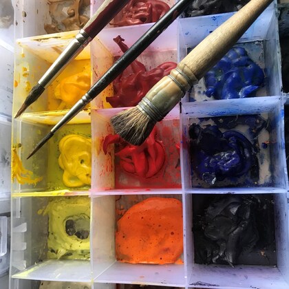 En närbild av en palett med olika färger och tre penslar ovanpå.