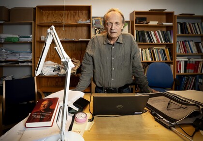 Person står vid ett skrivbord i ett kontor med böcker, papper och en laptop.