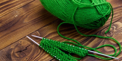 Grönt garnnystan och stickning på träbord med två stickor och påbörjat arbete.