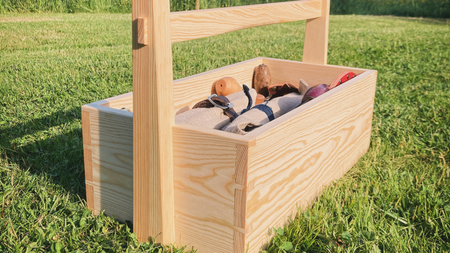 En trälåda med handtag står på gräsmatta, fylld med olika verktyg och föremål.