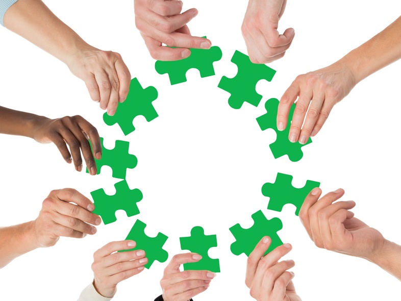 Flera händer håller gröna pusselbitar i en cirkel mot en vit bakgrund.