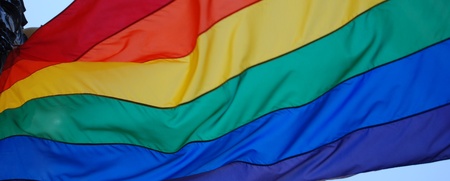 En regnbågsflagga vajar mot en blå himmel, symbol för HBTQ+-rörelsen.