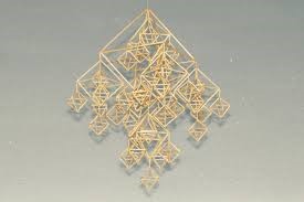 En geometrisk mobil av halm, bestående av flera sammanlänkade romber och trianglar, hänger mot en grå bakgrund.