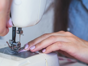 En person syr tyg med en symaskin, händerna syns tydligt vid arbetet.