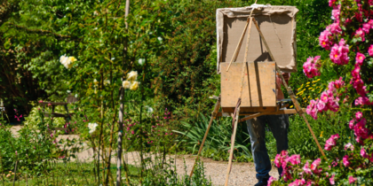 En person målar utomhus i en blomstrande trädgård, duken täcker ansiktet.