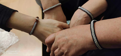 Fyra händer med likadana armband håller i varandra i en cirkel.