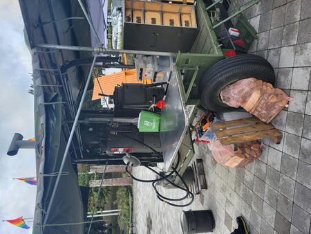 Militärt fältkök på hjul med vedträn, köksutrustning och regnskydd, utomhus på stenlagd yta.