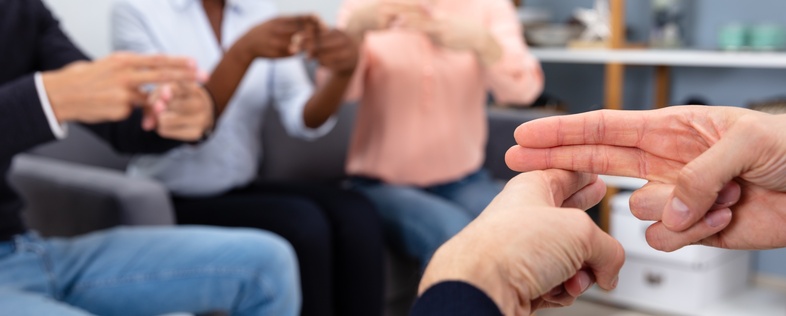 Fyra personer sitter i en cirkel och kommunicerar med teckenspråk, fokus på händerna.