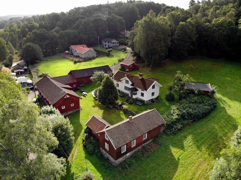 Flygfoto över en lantlig gård med flera röda och vita hus omgivna av grönska och skog.