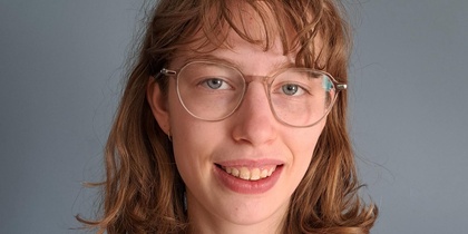 Person med axellångt brunt hår och blommig rödvit tröja mot grå bakgrund. Ansiktet är suddat.