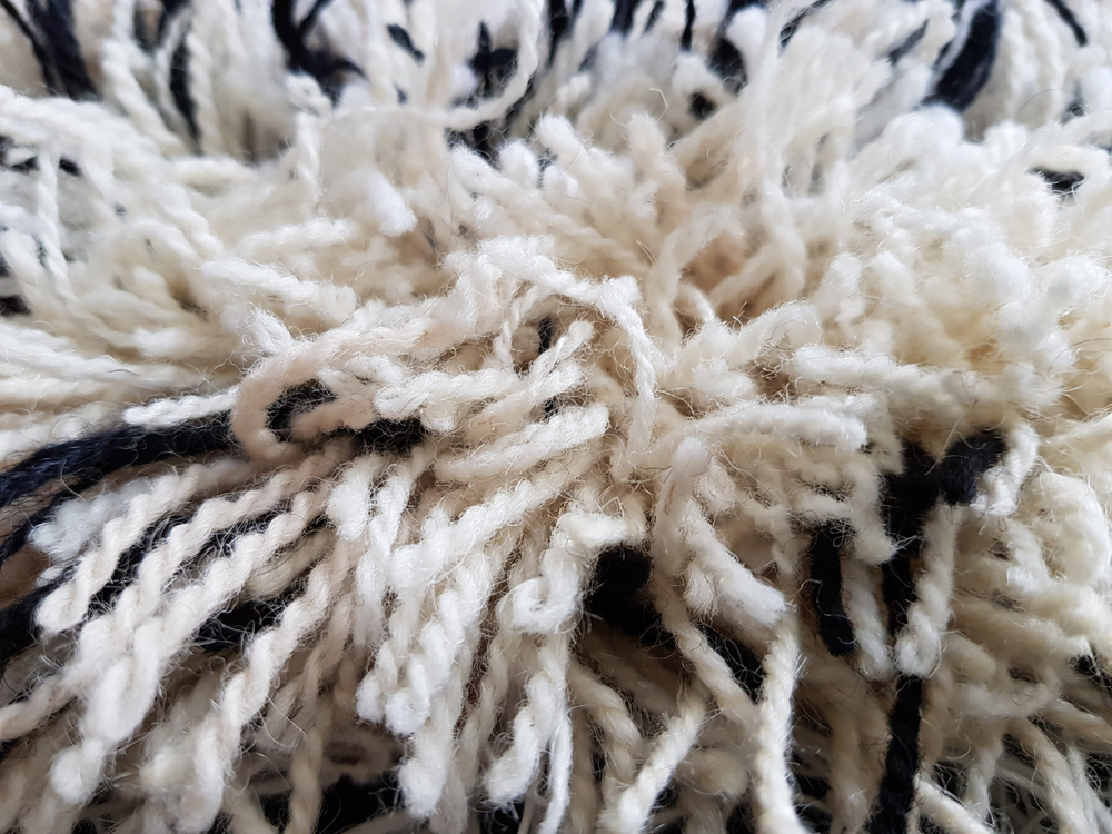 Närbild av en lurvig, vit och svart ullmatta med tjocka garntrådar.